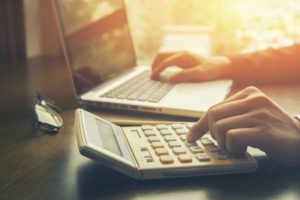 Person using calculator and laptop image for increase in probate court fees and changes to the excepted estate rules blog