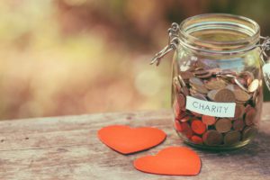 Pennies in a charity jar and hearts on wooden table image for leaving a gift to a charity in your will blog