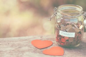 Pennies in a charity jar and hearts on wooden table image for blog on leaving a gift to a charity in your will
